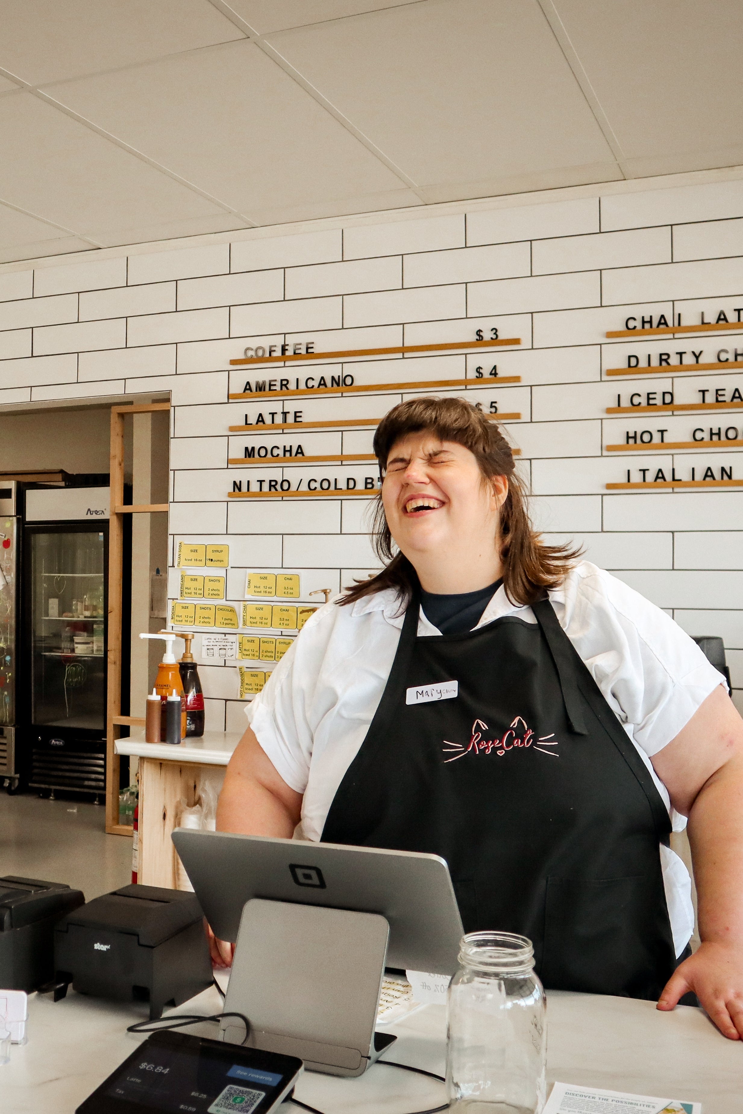 Rose Cat Coffee Co Barista, Mary Claire, smiles behind the counter while serving a customer. 