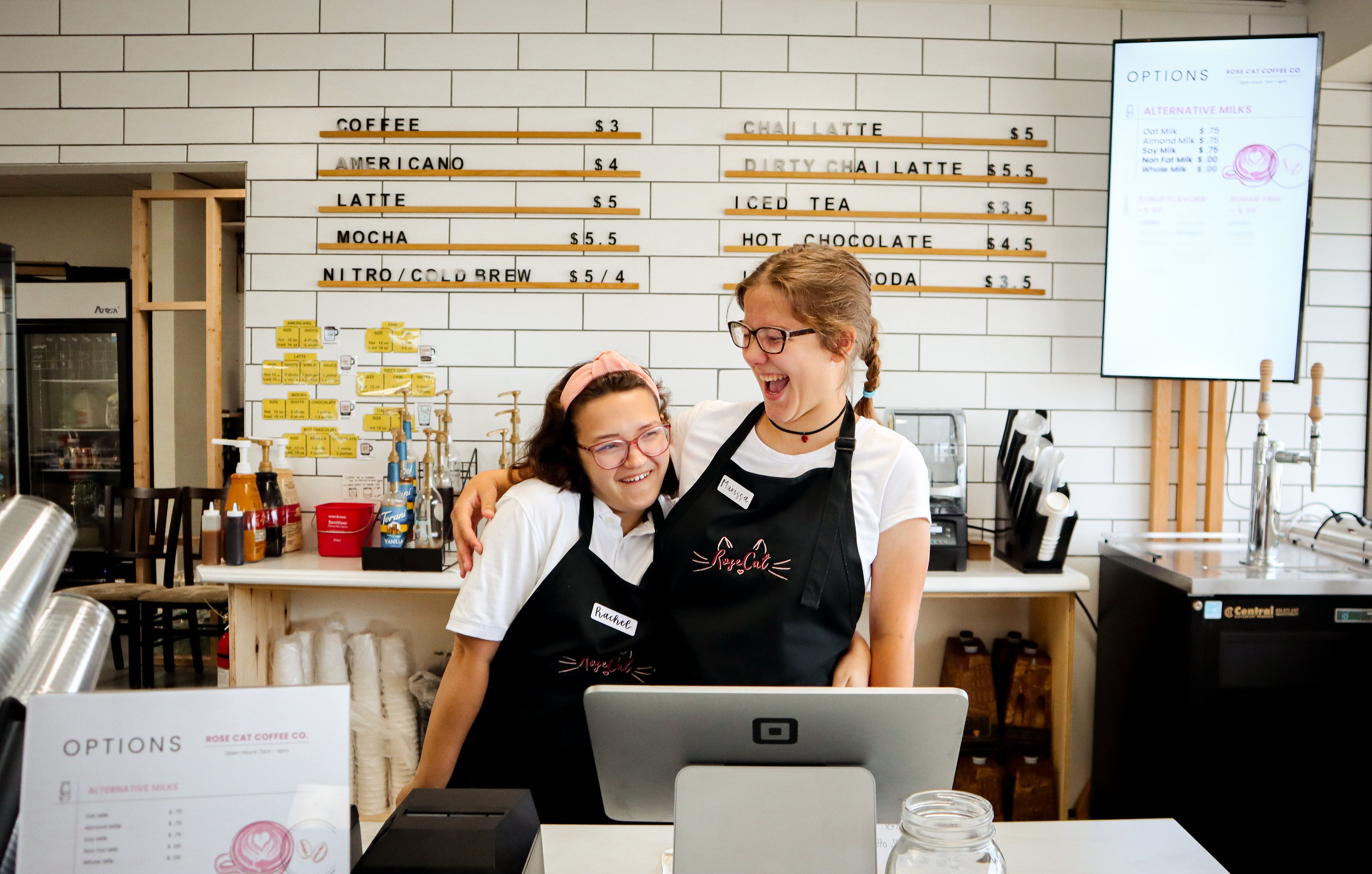 Rose Cat Baristas Rachel and Marissa embrace behind the counter with smiles on their faces!